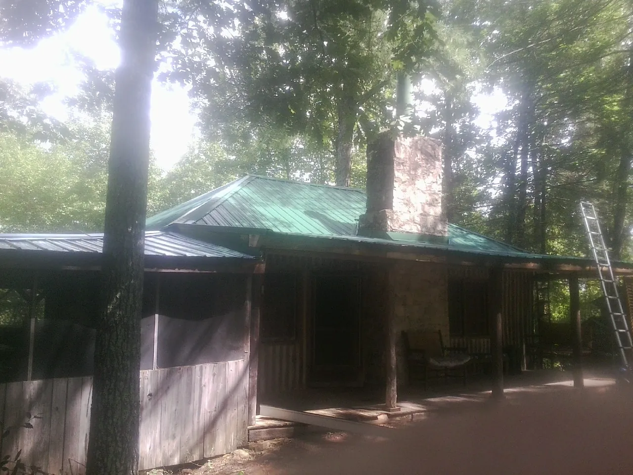 Green metal roof and stone chimney above a log cabin porch in Chatsworth