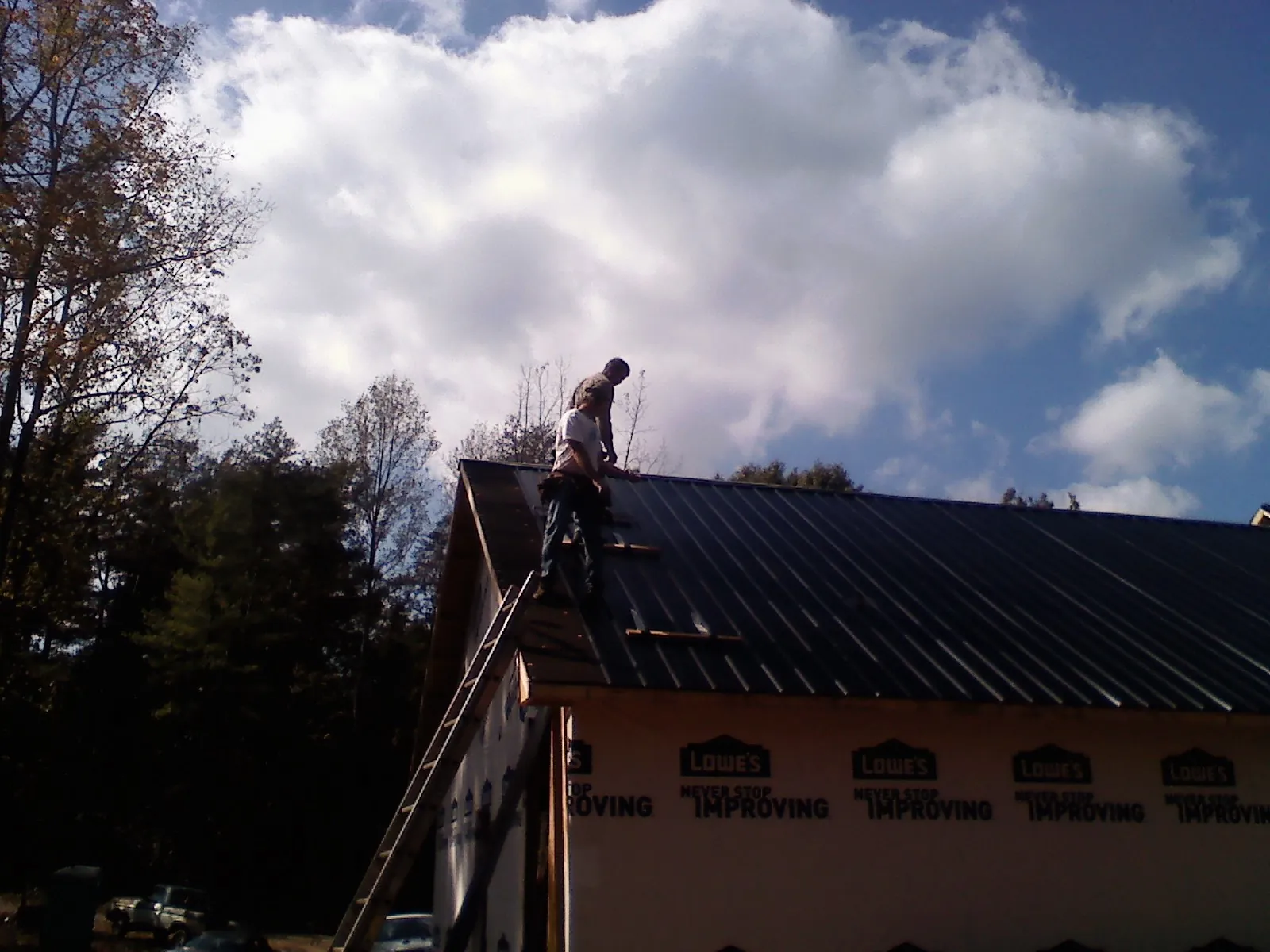 Roofer fastening dark metal panels high against a cloudy sky, from a Roof Inspection job in Chatsworth