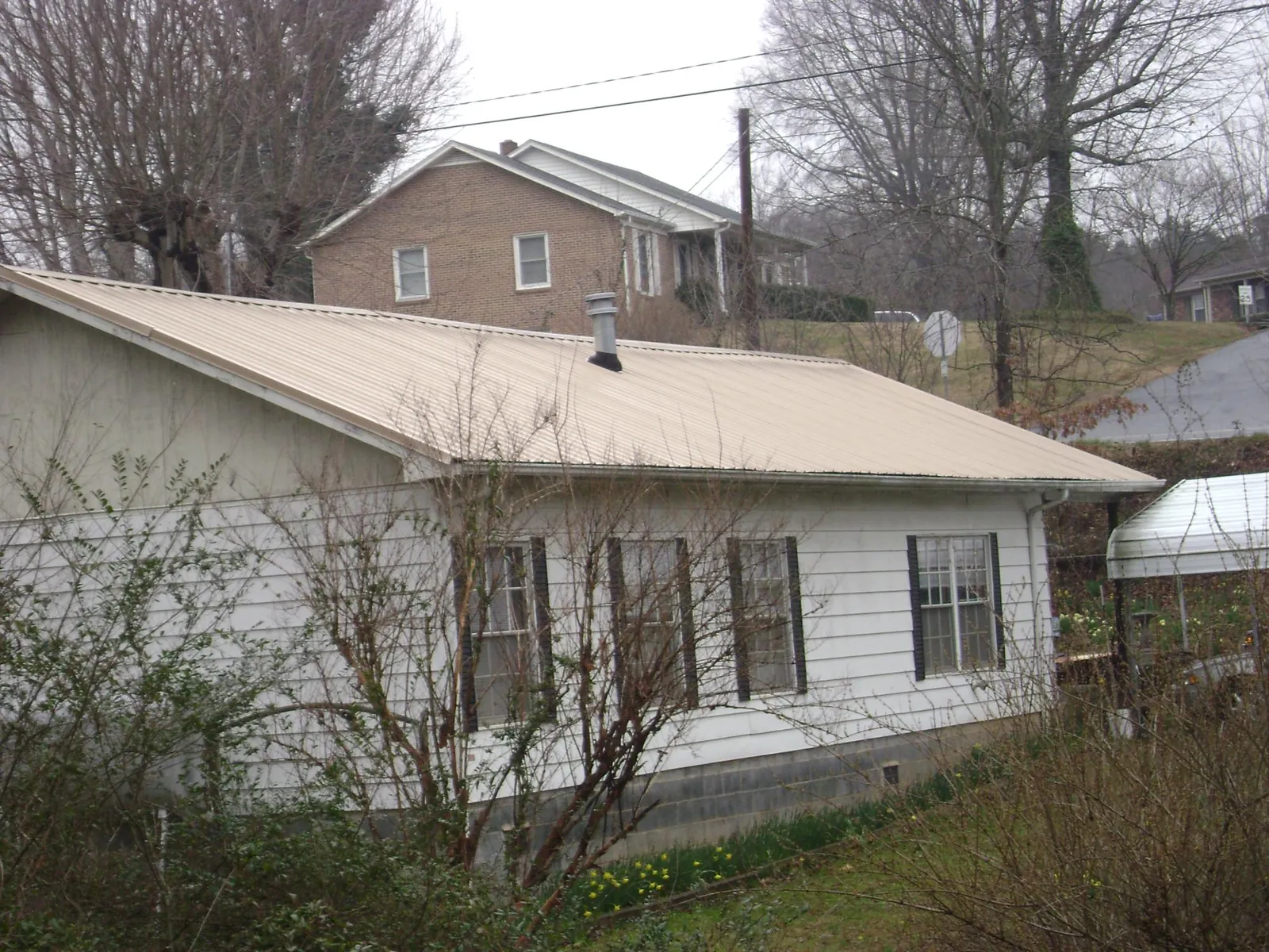 Tan metal roof on a white sided house set into a hillside — Commercial Roofing by Roofing Brothers in Chatsworth